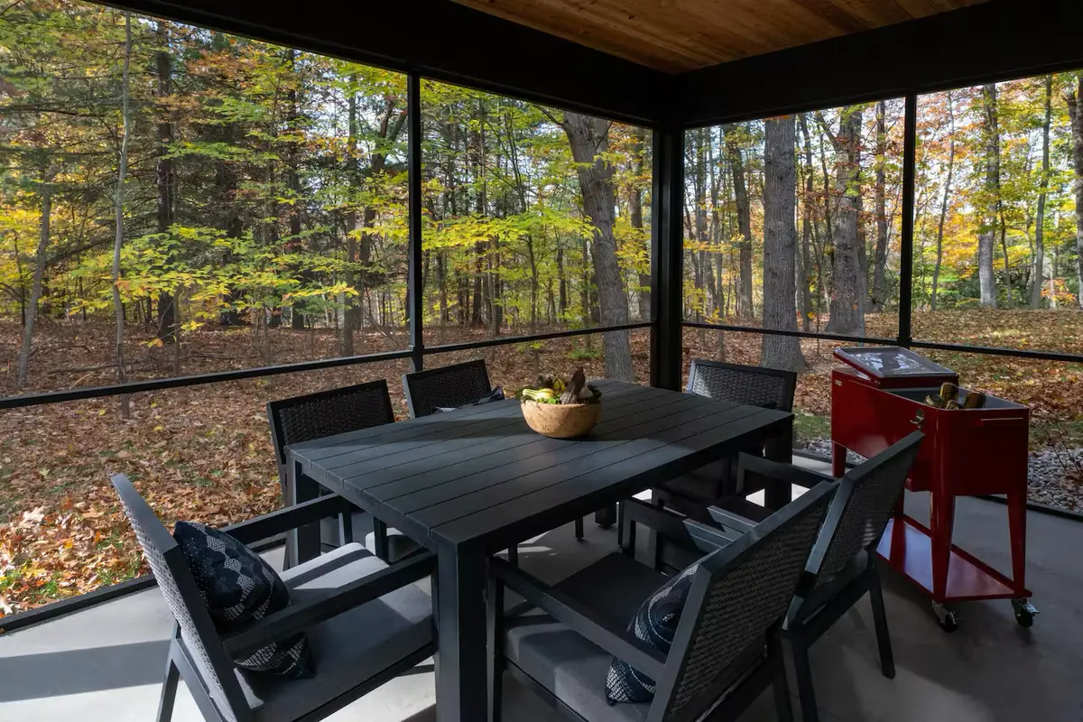 A long dining table on a screened porch that looks straight out into the autumn woods